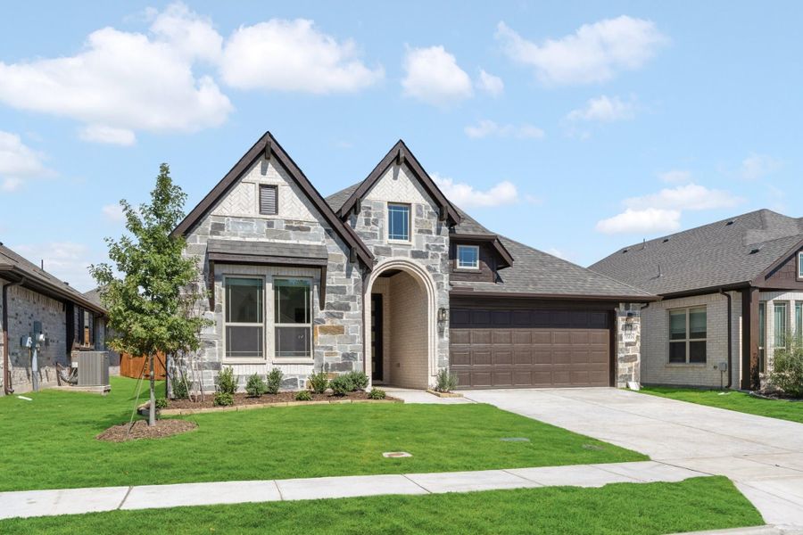 Single-story home with stone exterior, arched entry, two-car garage, and green front lawn