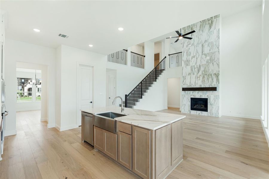 Open-concept kitchen with island, quartz countertops, and marble fireplace wall with staircase in background