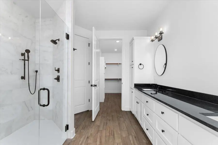 Bathroom with a marble finish shower, double vanity, wood finished floors, a walk in closet, and baseboards Bathroom with a marble finish shower, double vanity, wood finished floors, a walk in closet, and baseboards