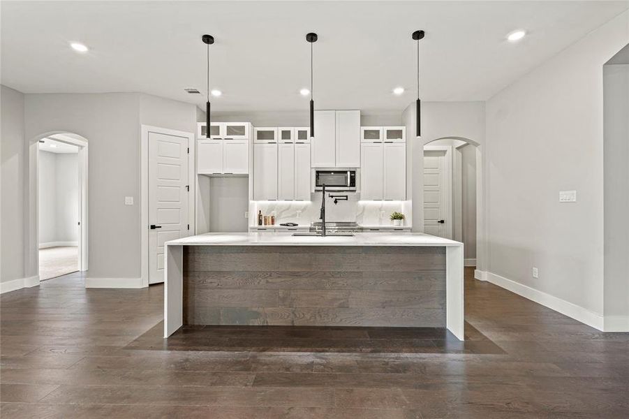 Kitchen featuring arched walkways, stainless steel microwave, dark wood finished floors, and recessed lighting