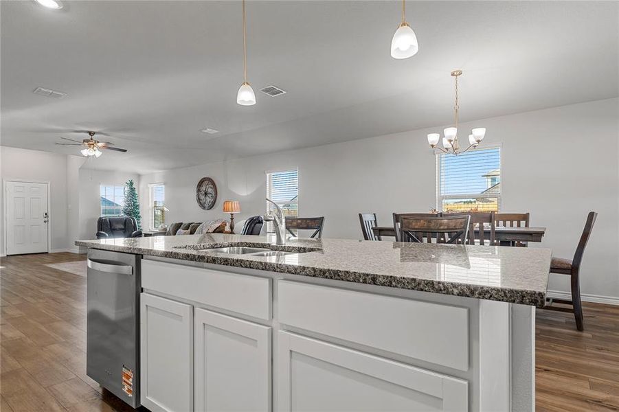 Kitchen featuring light wood-type flooring, white cabinets, light stone counters, and a kitchen island with sink