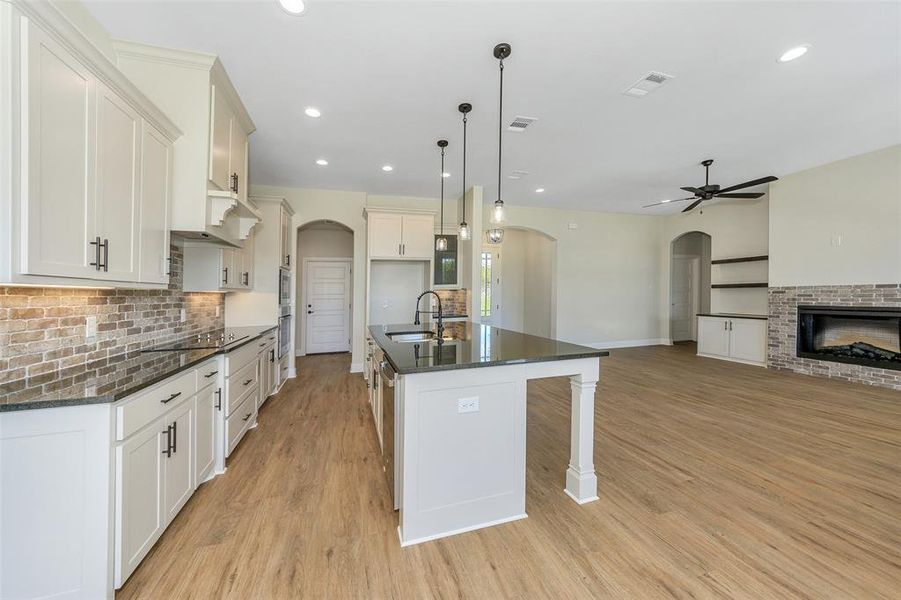 Kitchen with a kitchen island with sink, dark stone countertops, light hardwood / wood-style flooring, ceiling fan, and hanging light fixtures