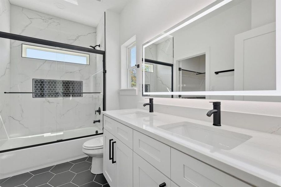 Full bathroom featuring shower / bath combination with glass door, double vanity, and dark tile patterned flooring Full bathroom featuring shower / bath combination with glass door, double vanity, and dark tile patterned flooring