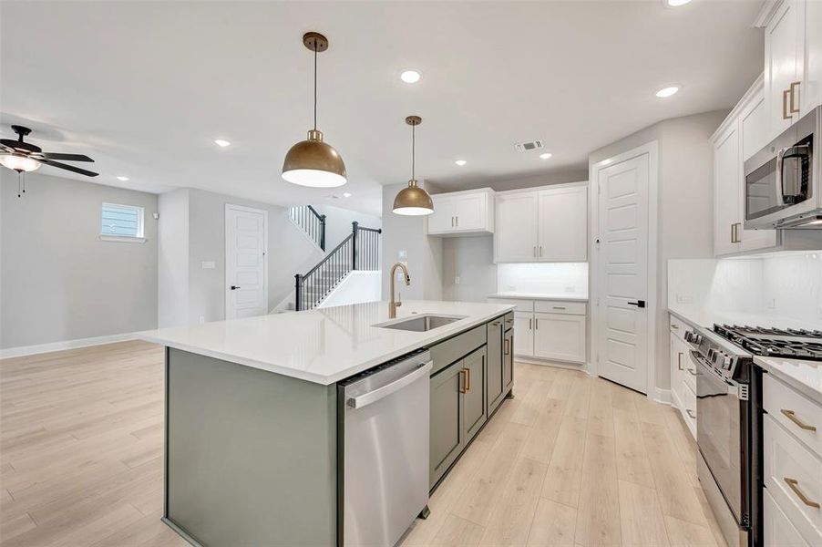Kitchen featuring stainless steel appliances, pendant lighting, an island with sink, ceiling fan, and light wood finished floors