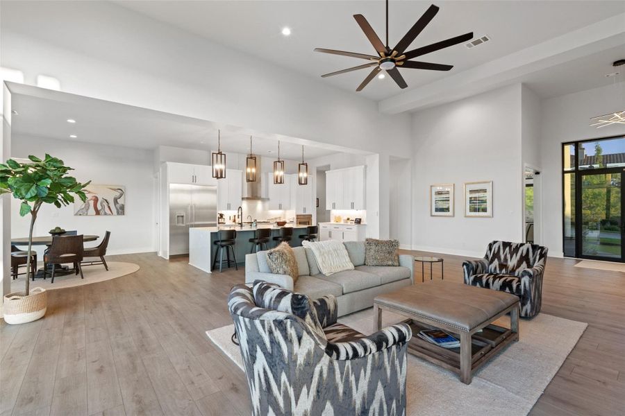 Open-concept interior featuring light wood-finish flooring, a contemporary kitchen with stainless steel appliances, a spacious living area with a ceiling fan, and high ceilings with recessed lighting