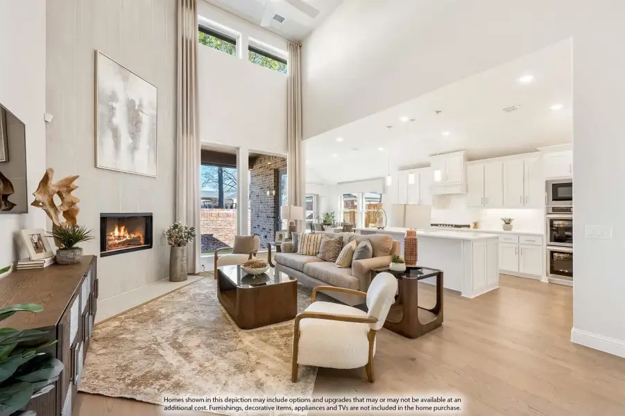 Open-concept living room with two-story ceiling, tile fireplace, and view into white kitchen with hardwood floors