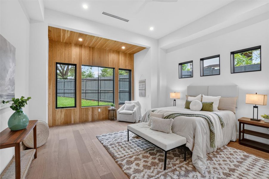 Sun-filled bedroom featuring wide plank flooring and a striking wood accent wall with expansive windows overlooking the yard.