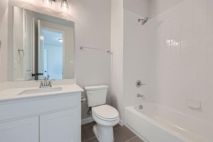 Full bathroom featuring toilet, tiled shower / bath combo, vanity, and tile patterned flooring