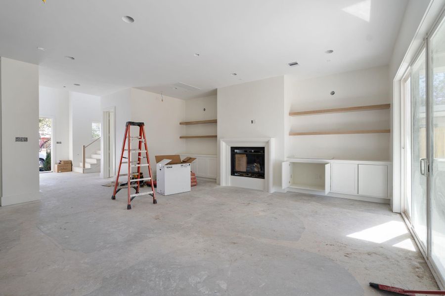 View from the kitchen into the living room, where the fireplace anchors the space and is framed by custom built in cabinetry and open shelving. Light pendants will be added above the shelving to complete the look.