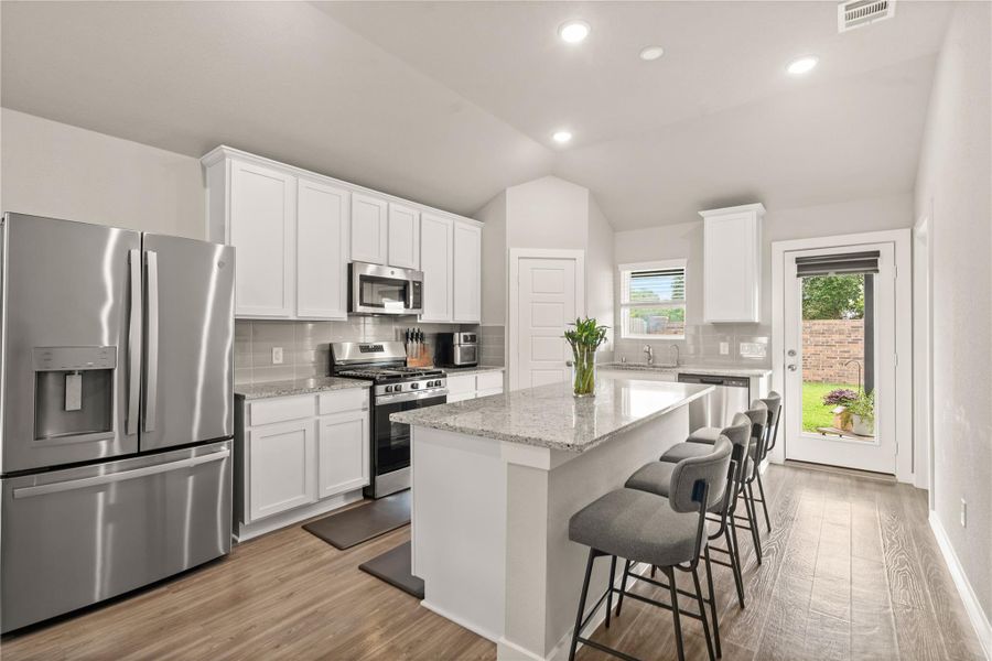 The stylish eat-in kitchen features sleek granite countertops, stainless steel appliances, abundant white cabinetry, and a spacious center island with bar seating.