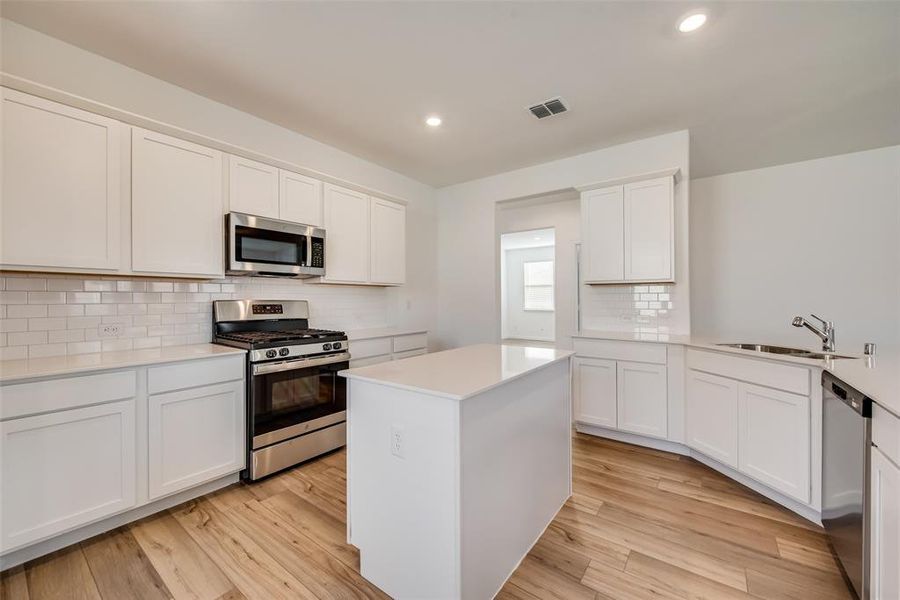 Kitchen with light wood-type flooring, appliances with stainless steel finishes, white cabinets, sink, and tasteful backsplash