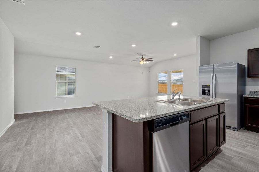 Kitchen with dark wood finish cabinetry, stainless steel appliances, open floor plan, a center island with sink, and light wood-style floors