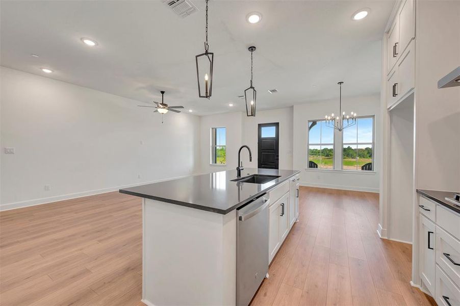 Open-concept living space featuring a central kitchen island with a black sink and faucet, integrated dishwasher, and pendant lighting Open-concept living space featuring a central kitchen island with a black sink and faucet, integrated dishwasher, and pendant lighting