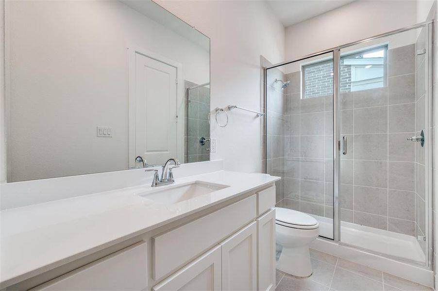 Bathroom featuring vanity, tile patterned flooring, toilet, and a shower with door