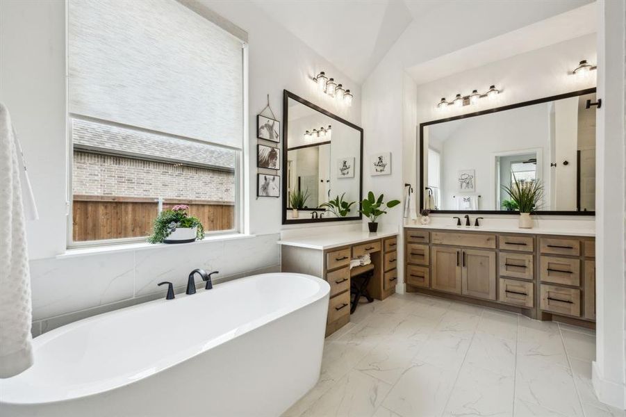 Full bathroom featuring healthy amount of natural light, marble look tiles, a soaking tub, vanity, and vaulted ceiling