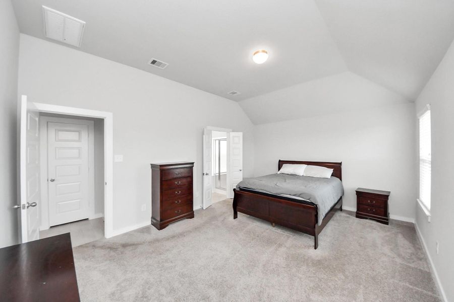 Generously sized primary bedroom with vaulted ceilings and plush carpeting, offering plenty of space for a full bedroom set and direct access to the private ensuite bathroom.