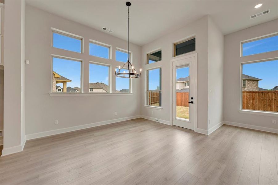Unfurnished dining area with a chandelier, light wood-type flooring, and healthy amount of natural light