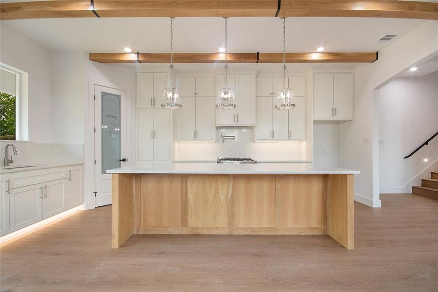 Kitchen featuring white cabinetry, hanging light fixtures, light wood finished floors, a large island, and light stone countertops
