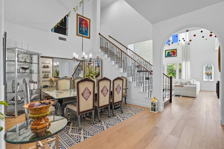 Dining room featuring stairway, a chandelier, light wood-style floors, and a towering ceiling