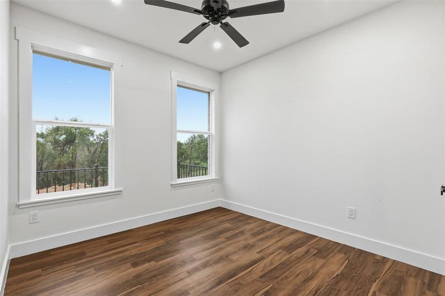 Room featuring wood-finish flooring, white baseboards, and bright white walls Room featuring wood-finish flooring, white baseboards, and bright white walls