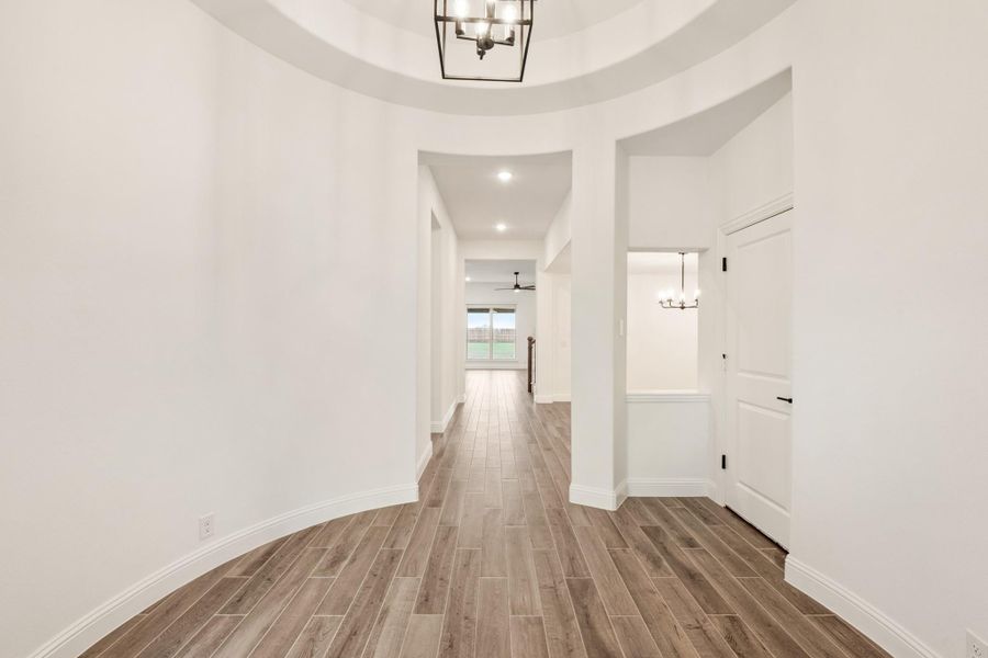 Curved foyer with tray ceiling, pendant chandelier, and wood-look tile floors leading to main hallway