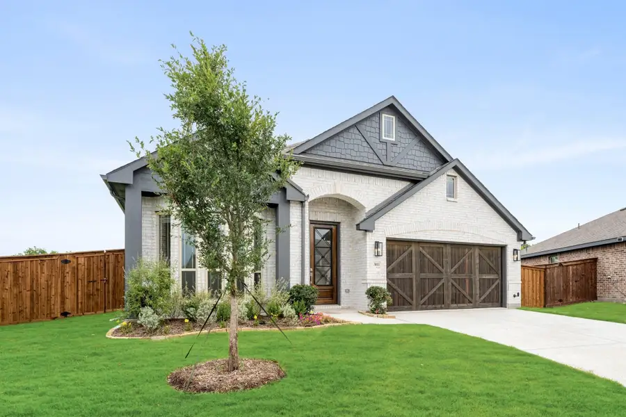 Single-story home with white brick exterior, arched entry, wood garage door, and landscaped front yard with young tree. Single-story home with white brick exterior, arched entry, wood garage door, and landscaped front yard with young tree.
