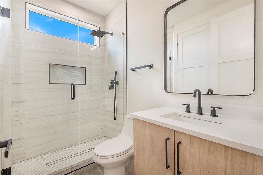 Bathroom featuring a shower with shower door, vanity, and toilet