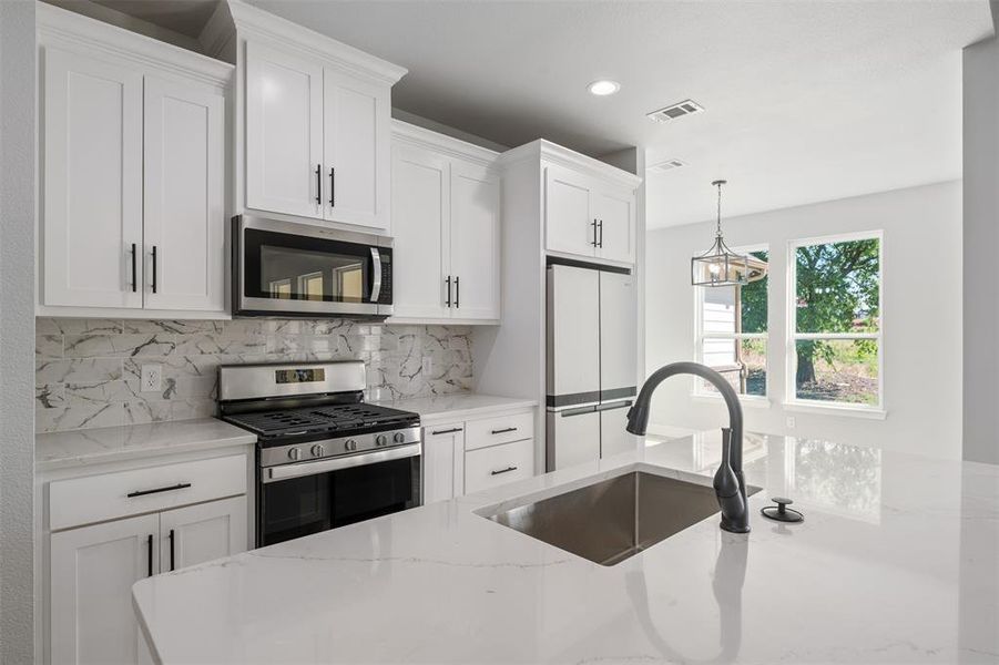 Kitchen with appliances with stainless steel finishes, backsplash, white cabinets, light stone counters, and pendant lighting Kitchen with appliances with stainless steel finishes, backsplash, white cabinets, light stone counters, and pendant lighting