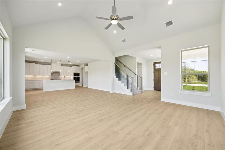 Unfurnished living room with recessed lighting, light wood-style flooring, high vaulted ceiling, a ceiling fan, and stairs