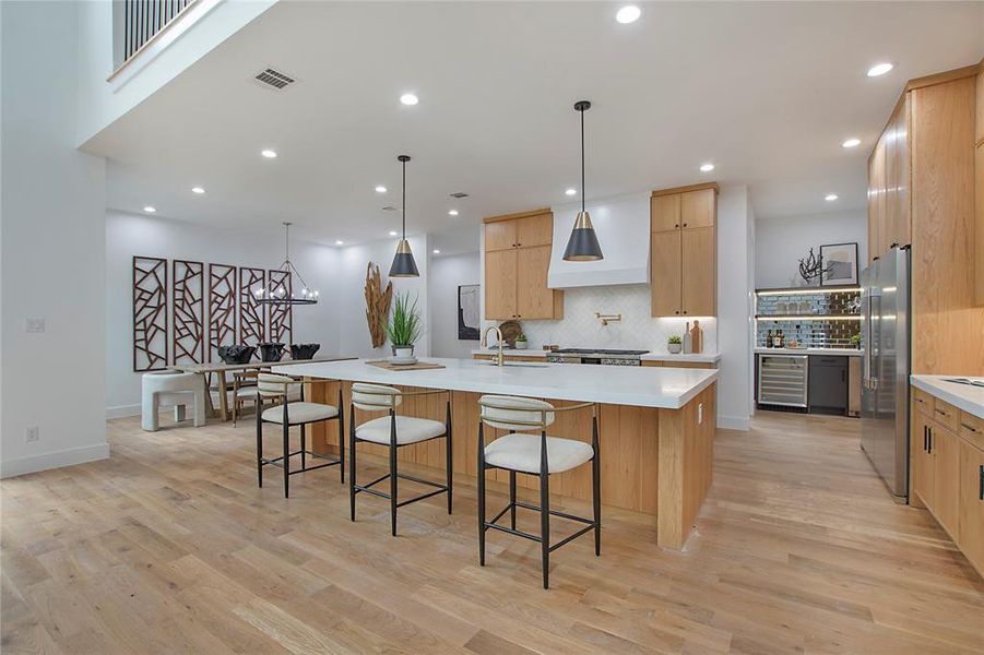 Kitchen featuring a large island, pendant lighting, high quality fridge, and light hardwood / wood-style floors