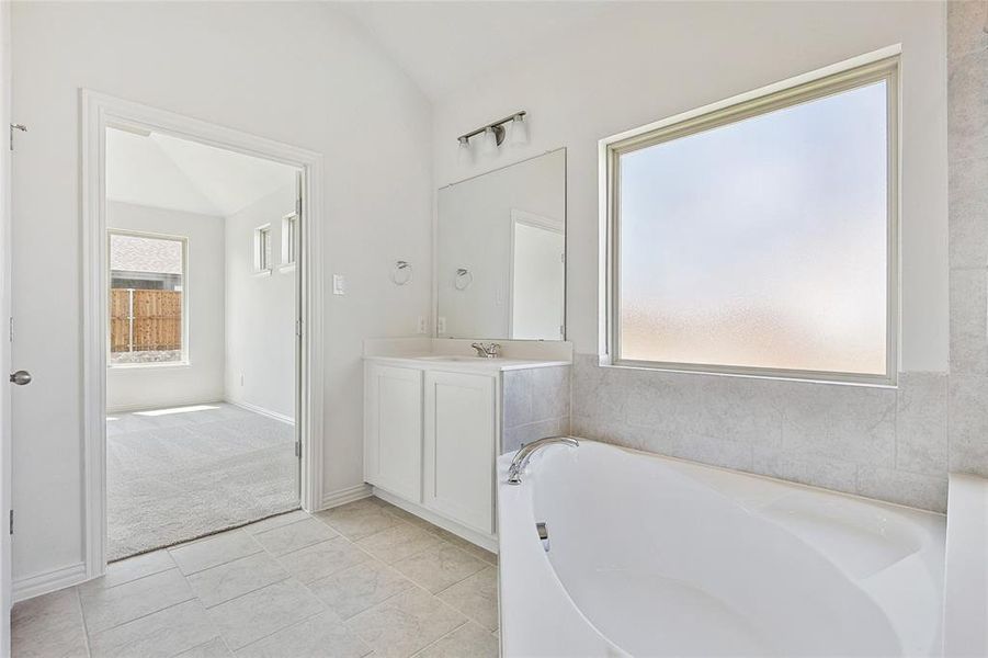 Bathroom with a bathtub, lofted ceiling, tile patterned flooring, and vanity