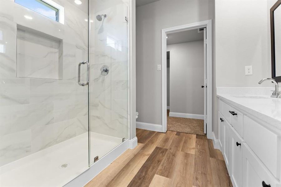 Full bathroom with a marble finish shower, wood finished floors, vanity, baseboards, and toilet Full bathroom with a marble finish shower, wood finished floors, vanity, baseboards, and toilet