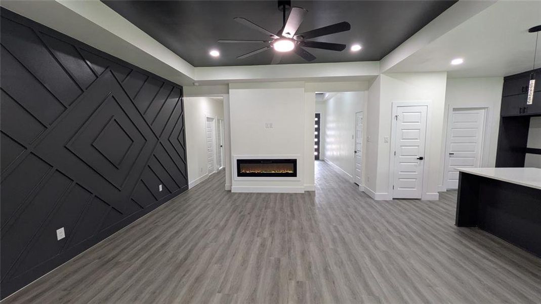 Unfurnished living room with a glass covered fireplace, light wood-style floors, baseboards, ceiling fan, and recessed lighting