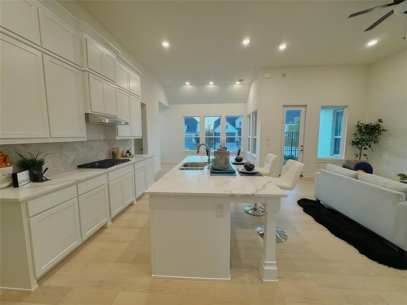 Kitchen with light stone countertops, sink, backsplash, an island with sink, and stainless steel gas stovetop