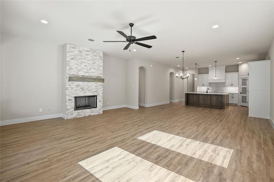 Unfurnished living room featuring arched walkways, a ceiling fan, a chandelier, light wood-type flooring, and a fireplace
