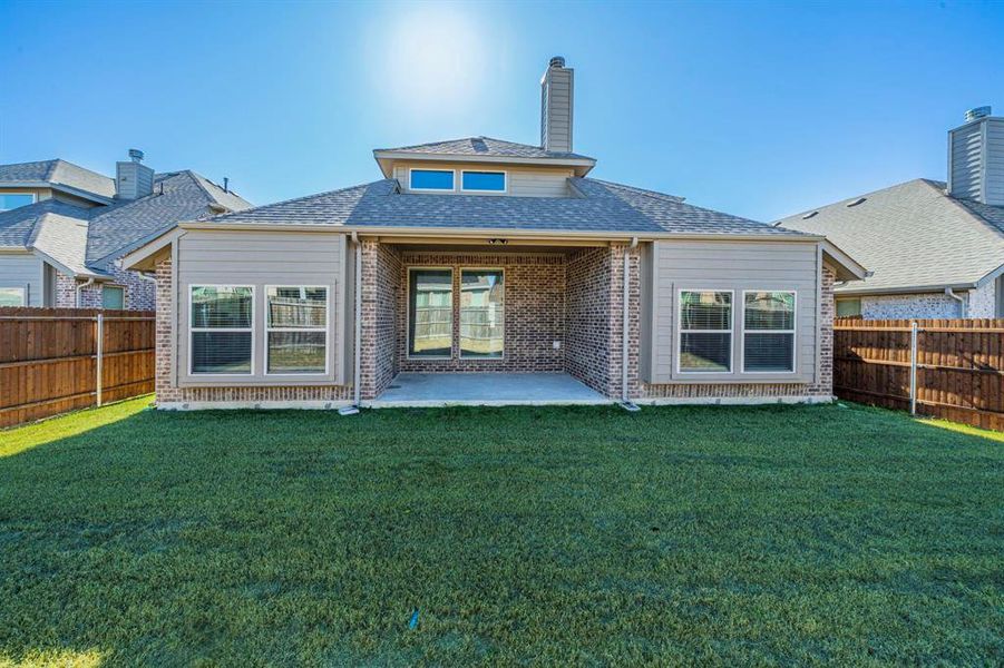 Expansive backyard featuring a manicured lawn, wood fencing, covered patio, and brick exterior with siding accents
