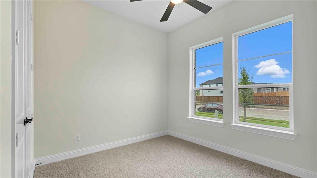 Bright interior room featuring two tall windows, light neutral wall paint, white trim, textured carpeting, and a ceiling fan with integrated lighting