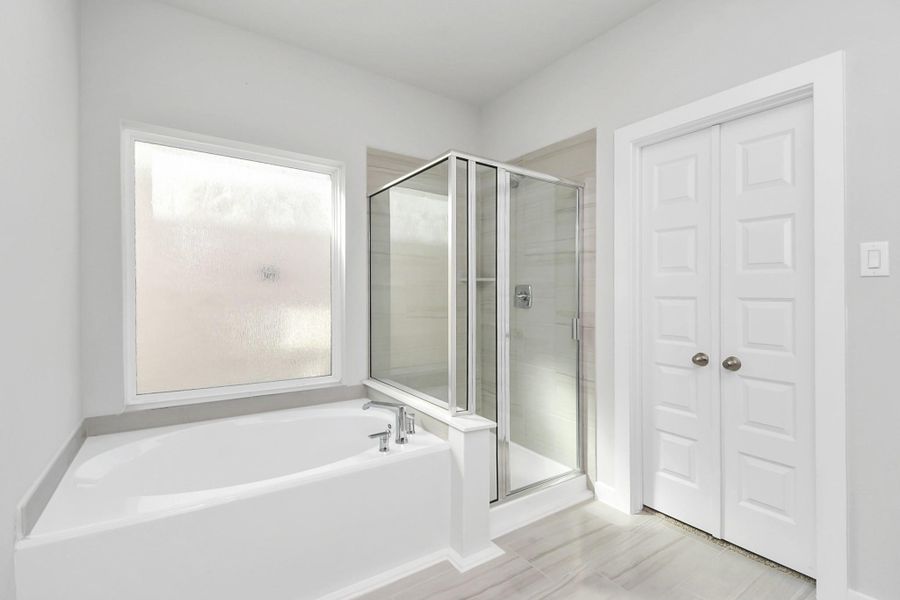 Escape to a spa-like oasis in this primary bathroom. Enjoy a walk-in shower with tile surround, a separate garden tub with custom detailing, and an elegant vanity featuring light countertops, modern hardware, and beautiful recessed lights. Sample photo of completed home with similar floor plan. Actual colors and selections may vary.