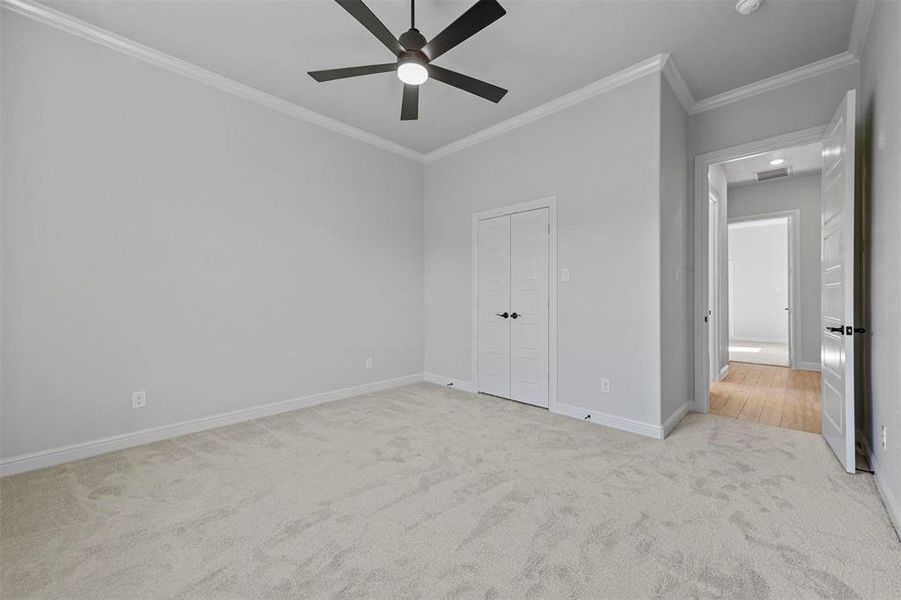 Unfurnished bedroom with ceiling fan, light colored carpet, crown molding, and a closet