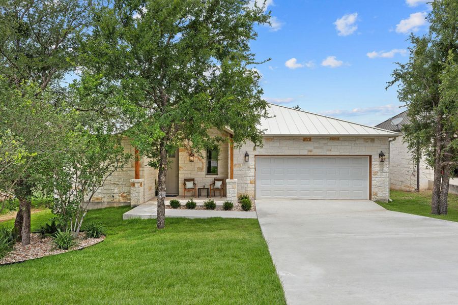 View of front of house with a standing seam metal roof, concrete driveway, stone siding, a garage, and a front yard View of front of house with a standing seam metal roof, concrete driveway, stone siding, a garage, and a front yard