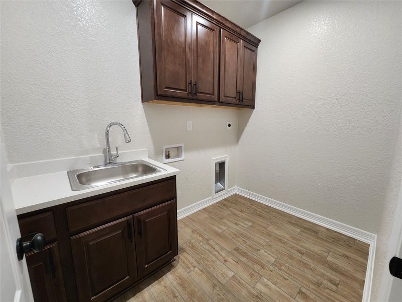 Functional laundry space featuring convenient sink, rich cabinetry, and durable wood-look flooring. Functional laundry space featuring convenient sink, rich cabinetry, and durable wood-look flooring.
