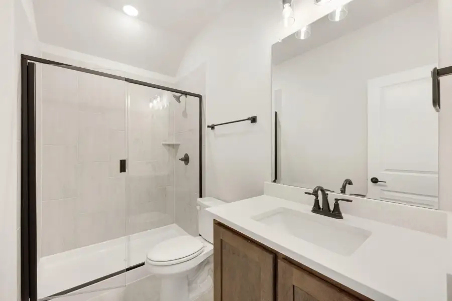 Bathroom with tiled shower, wood vanity, white countertop, and black fixtures