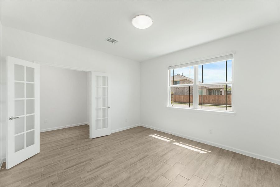 Empty room with wood-look tile floors, white walls, French doors, and a large window with backyard view.