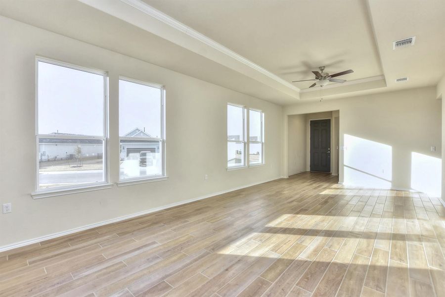 Empty room featuring a tray ceiling, a ceiling fan, visible vents, and light wood finished floors