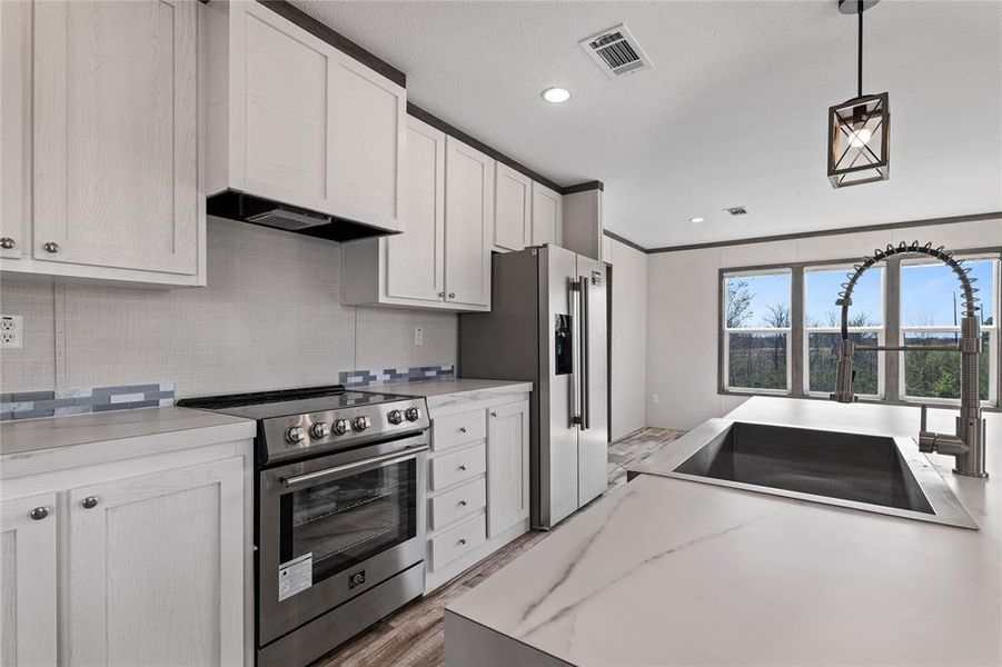 Kitchen with stainless steel appliances, light countertops, ornamental molding, hanging light fixtures, and light wood-style flooring