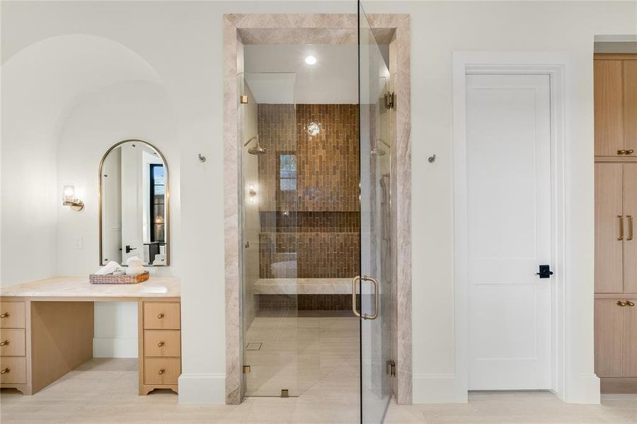 Glass-enclosed shower with floor-to-ceiling brown mosaic tile, dual shower heads, and built-in bench