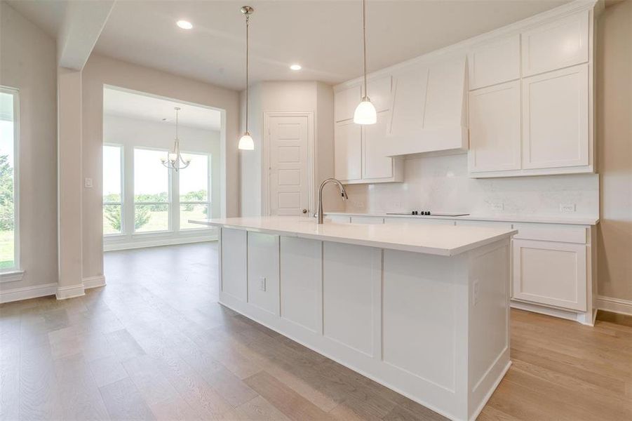 Kitchen featuring custom range hood, light hardwood / wood-style floors, decorative backsplash, white cabinetry, and a kitchen island with sink