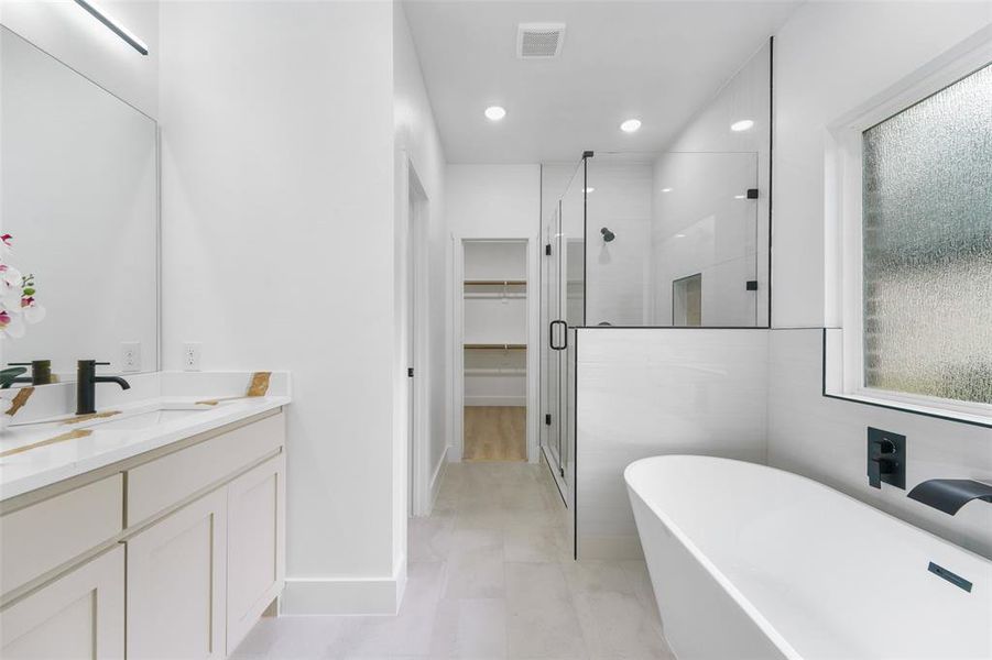 Contemporary bathroom featuring a freestanding soaking tub with a matte black wall-mounted faucet, a frameless glass shower enclosure, a vanity with a quartz-finish countertop and undermount sink, and light-toned tile flooring Contemporary bathroom featuring a freestanding soaking tub with a matte black wall-mounted faucet, a frameless glass shower enclosure, a vanity with a quartz-finish countertop and undermount sink, and light-toned tile flooring
