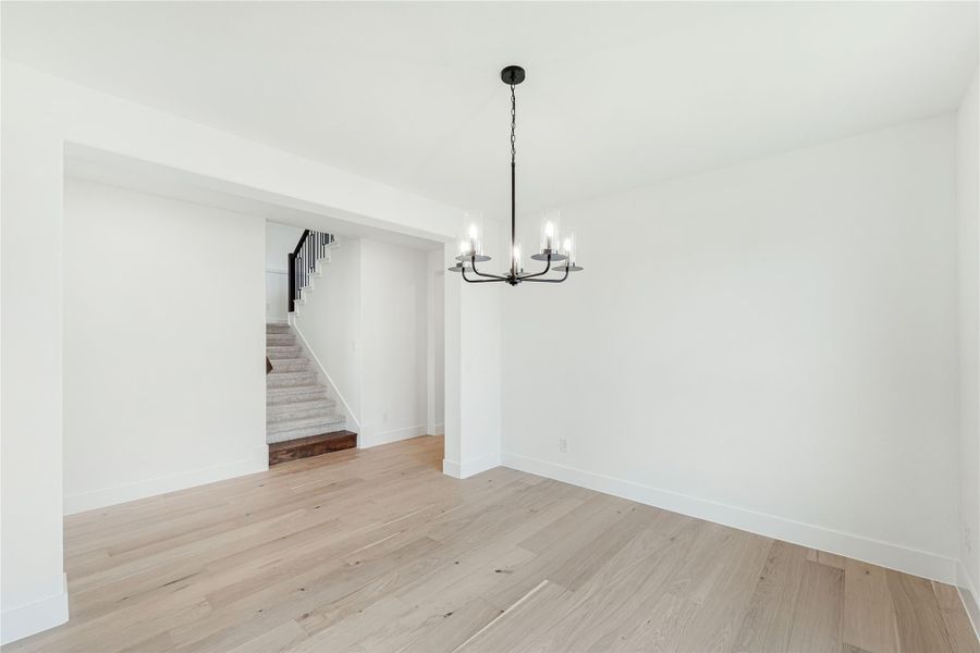 Empty dining room with light hardwood floors, black chandelier, and staircase visible through doorway Empty dining room with light hardwood floors, black chandelier, and staircase visible through doorway