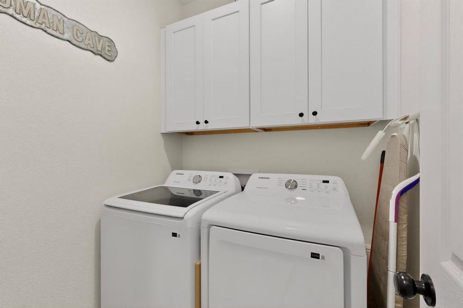 Laundry area featuring white shaker-style cabinetry with black hardware, complementing a neutral wall finish